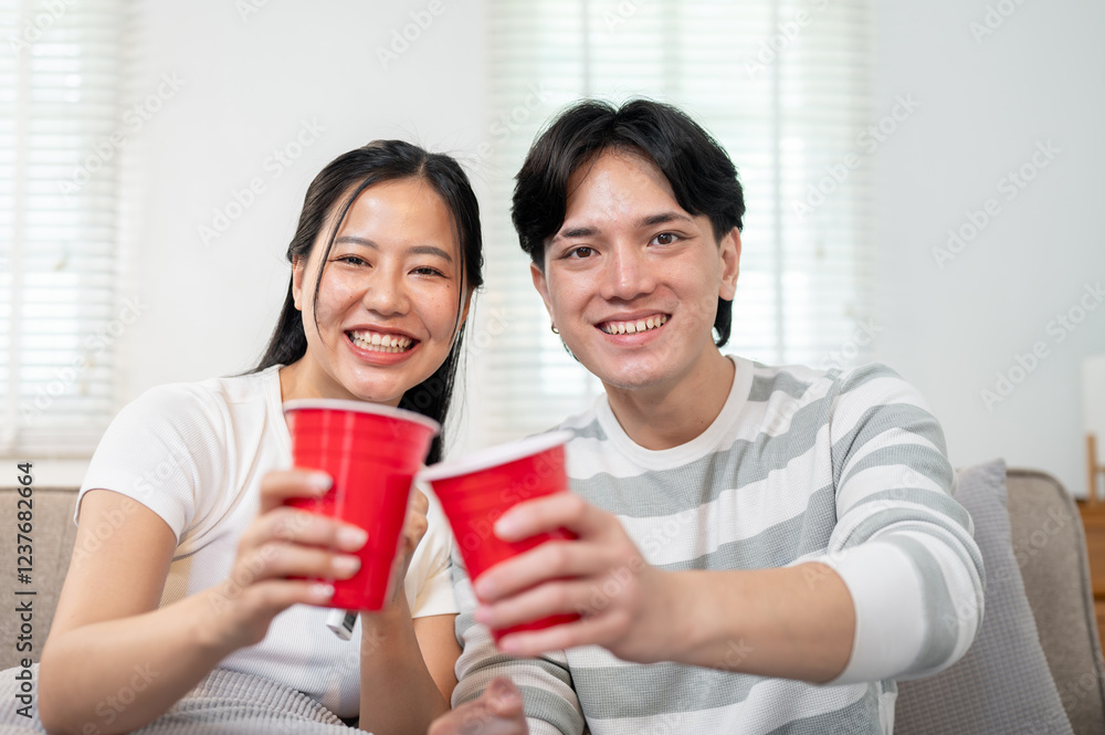 A close-up of a couple clinking red disposable plastic cups while watching a football match at home. A close-up of a couple clinking red disposable plastic cups while watching a football match at home.