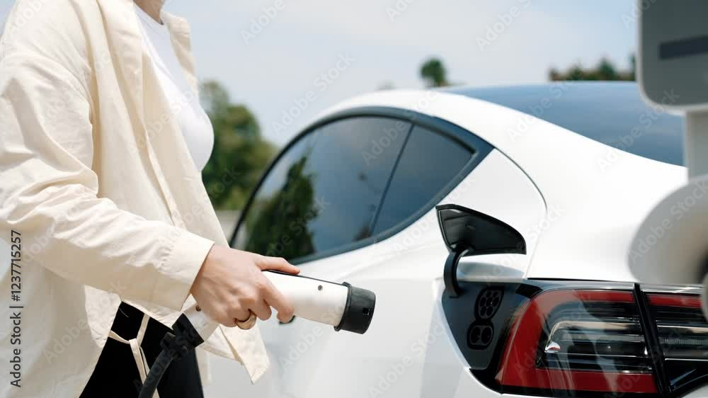 Slow motion woman put EV charger to recharge electric car's battery from charging station. Alternative energy and rechargeable EV car for sustainable environmental friendly travel concept. Expedient