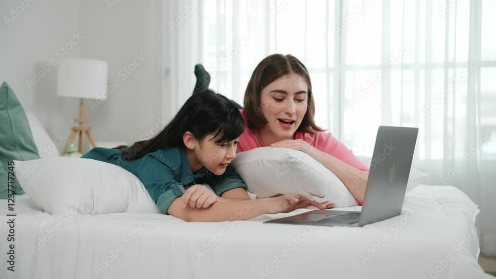 Attractive daughter and caucasian mother watching movie at laptop screen while lie on bad. Happy family spend time together before bed time. Parent and cute girl enjoy playing games together Pedagogy. Attractive daughter and caucasian mother watching movie at laptop screen while lie on bad. Happy family spend time together before bed time. Parent and cute girl enjoy playing games together Pedagogy.