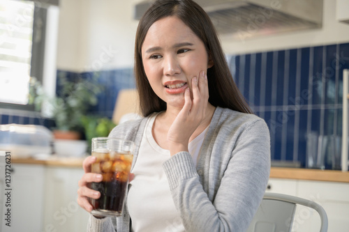 Young Asian woman touching her cheek and mouth feeling pain from toothache, decay or sensitivity cavity molar tooth or inflammation cause by drink cold, sparkling water. Food and health care concept. photo