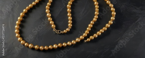 Overhead view of a single strand golden color pearl necklace on rough black slate, golden, earthy photo