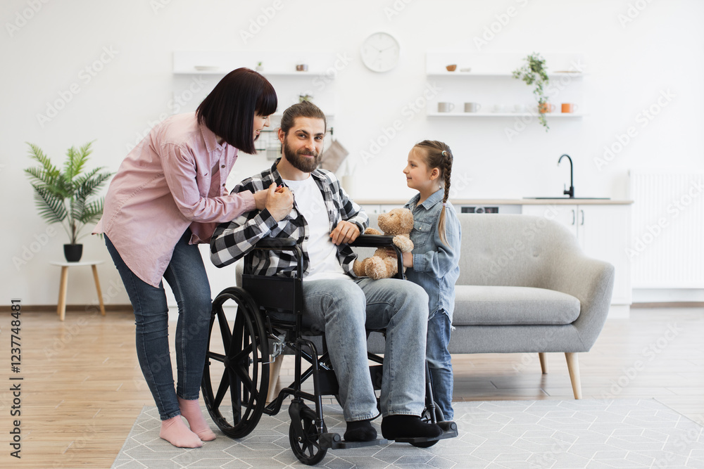 Caucasian family with father in wheelchair interacting warmly with mother and young daughter. Modern kitchen creates welcoming atmosphere. Captures family love, support, and disability awareness. Caucasian family with father in wheelchair interacting warmly with mother and young daughter. Modern kitchen creates welcoming atmosphere. Captures family love, support, and disability awareness.