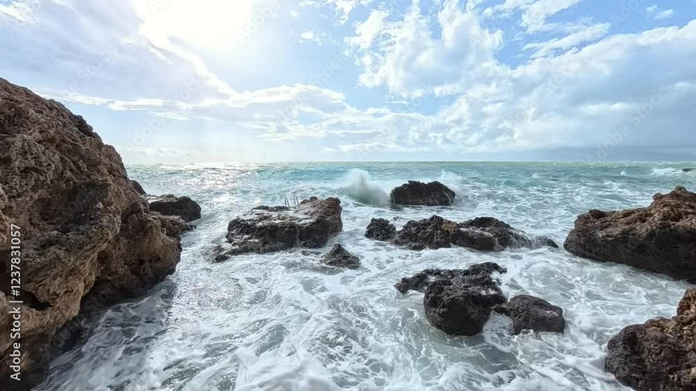 A wide-angle slow-motion view of foamy waves surging between jagged rocks, with the sun shining brightly and reflecting off the water under a picturesque sky A wide-angle slow-motion view of foamy waves surging between jagged rocks, with the sun shining brightly and reflecting off the water under a picturesque sky
