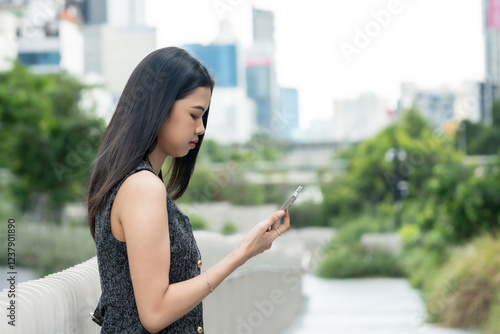 Lifestyle of beautiful Asian female office worker checking smartphone while standing on elevated walkway in urban business center. Wearing elegant black vest with white skirt, appearing on work. Free Download Lifestyle of beautiful Asian female office worker checking smartphone while standing on elevated walkway in urban business center. Wearing elegant black vest with white skirt, appearing on work. - GFXLoad