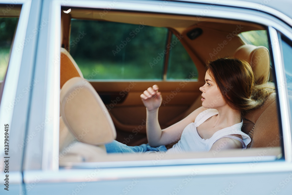 Naklejka premium Young woman relaxing in a car, wearing casual clothes, enjoying peaceful moments in nature with soft sunlight illuminating her face and a serene background.