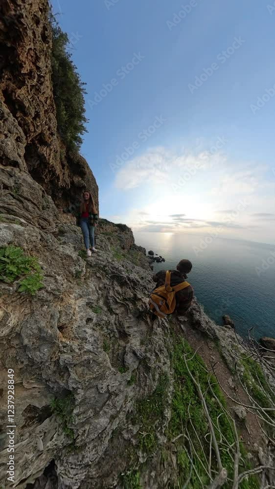 Vertical video. A Male and Female Traveler Navigating Down a Rocky Cliffside Toward the Sea, With Rugged Terrain and Vegetation Surrounding Them and the Vast Ocean Beyond. Coastal Exploration Vertical video. A Male and Female Traveler Navigating Down a Rocky Cliffside Toward the Sea, With Rugged Terrain and Vegetation Surrounding Them and the Vast Ocean Beyond. Coastal Exploration