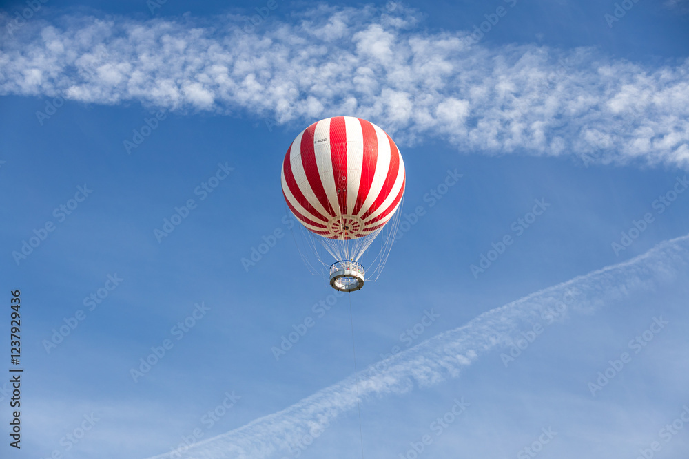 A vibrant red-and-white hot air balloon floating in a clear blue sky over Budapest, Hungary, offering an adventurous and serene aerial perspective.