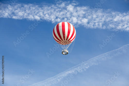 A vibrant red-and-white hot air balloon floating in a clear blue sky over Budapest, Hungary, offering an adventurous and serene aerial perspective.