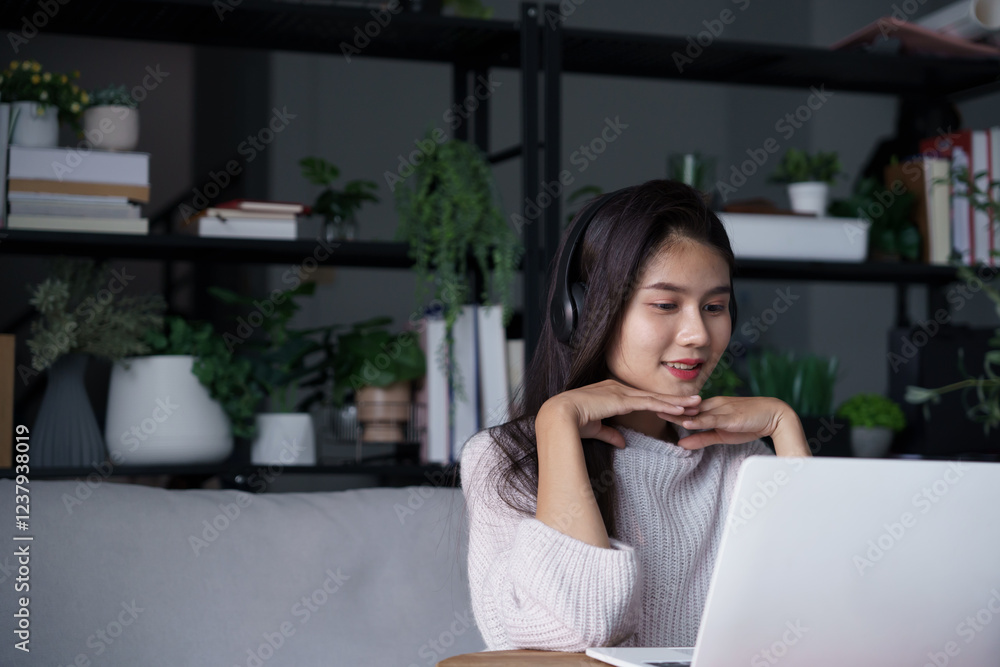 Asian woman sits on sofa wearing headphone watching movie on laptop in living room Asian woman sits on sofa wearing headphone watching movie on laptop in living room