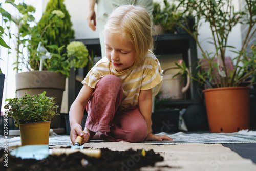 Blond girl planting plants indoors with another person, enjoying a sustainable lifestyle photo