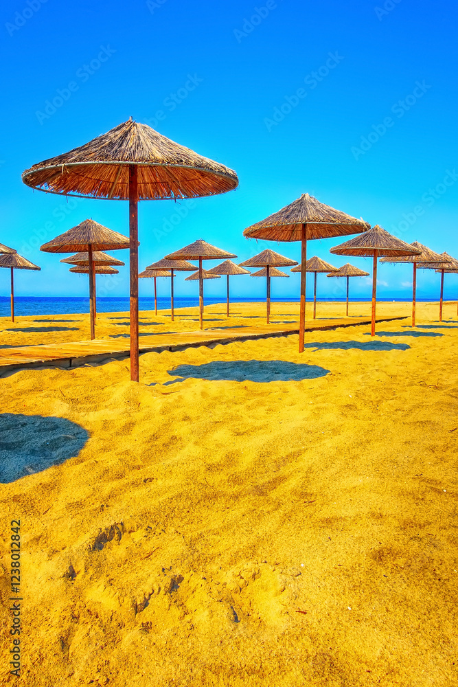 Fototapeta premium Row of wooden umbrellas at sandy beach, sea