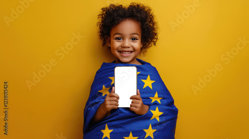 A cute little girl is holding a phone with a white screen on a yellow background. The child is wrapped in the flag of Europe. Phone mockup. The concept of celebrating Europe Day on May 9th photo