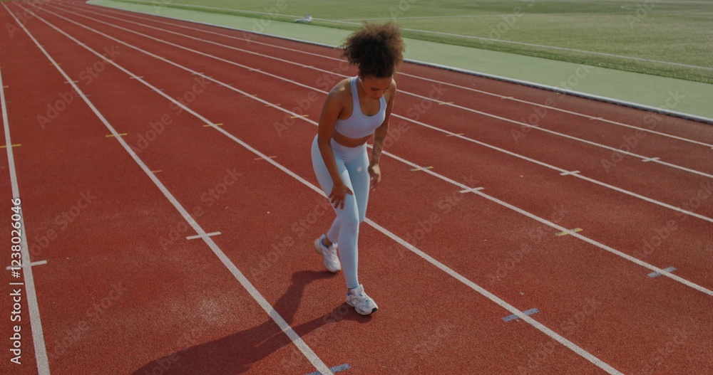 Obraz premium A woman in sports clothes and with earbuds in her ears does exercises standing at the stadium on a summer day