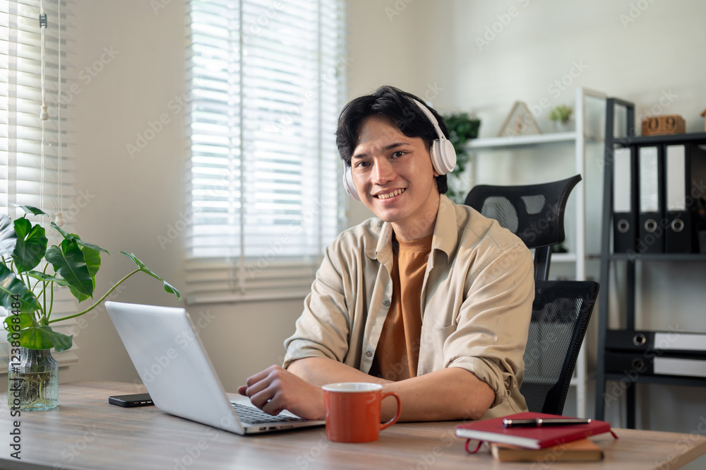 A creative Asian businessman is sitting in front of a laptop in his office, smiling at the camera. A creative Asian businessman is sitting in front of a laptop in his office, smiling at the camera.