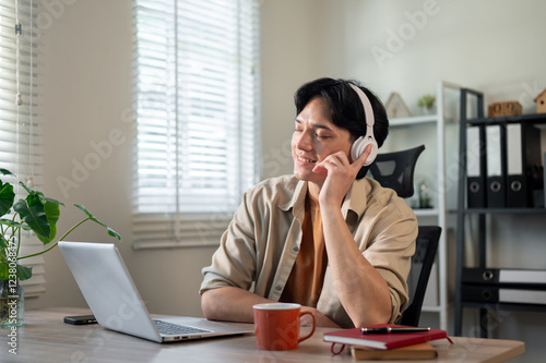 A carefree Asian businessman is enjoying the music on his headphones at his desk in the office.