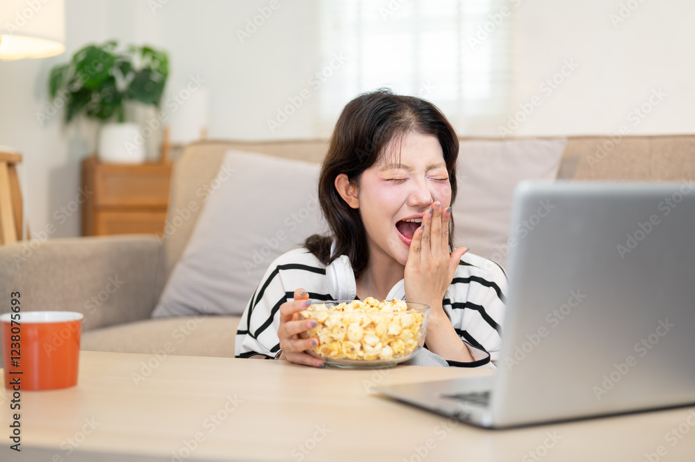 A woman enjoys eating popcorn while watching a movie on her laptop, having a fun time at home. A woman enjoys eating popcorn while watching a movie on her laptop, having a fun time at home.