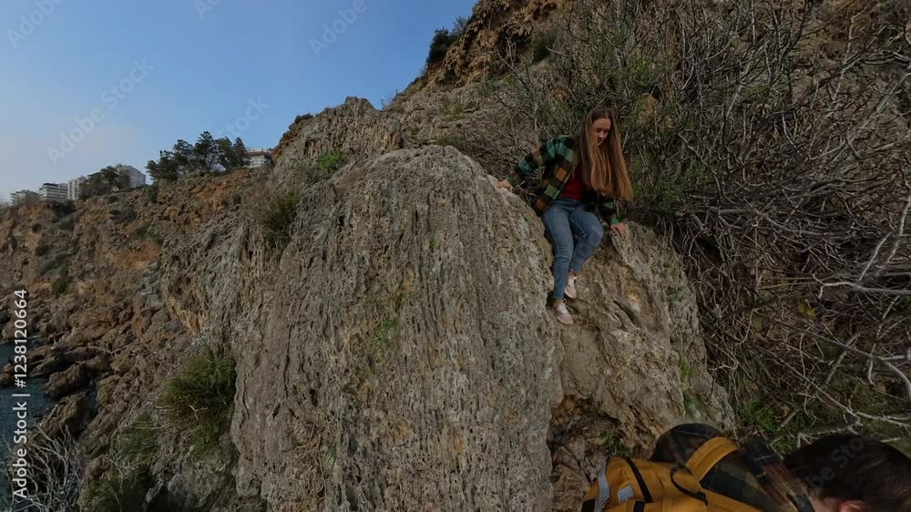 A Male Traveler Offering a Helping Hand to a Female Traveler Climbing Down a Rocky Cliff Path, With Vegetation and Jagged Rocks Surrounding Them. Supportive Coastal Descent A Male Traveler Offering a Helping Hand to a Female Traveler Climbing Down a Rocky Cliff Path, With Vegetation and Jagged Rocks Surrounding Them. Supportive Coastal Descent