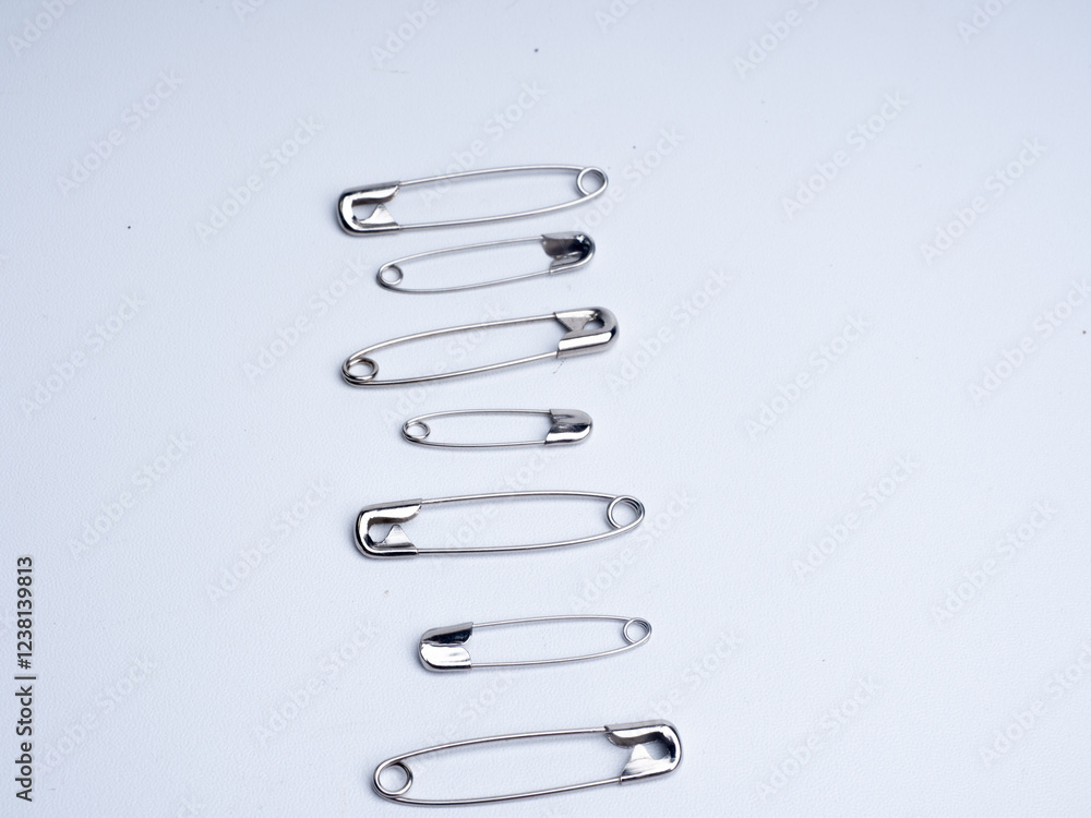 metallic safety pins attached to a larger safety pin, displayed against a white background.. A pile of shiny stainless steel safety pins on a white background.
metallic safety pins attached to a larger safety pin, displayed against a white background.. A pile of shiny stainless steel safety pins on a white background.