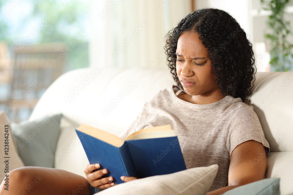 Disgusted black woman reading a paper book on a sofa Disgusted black woman reading a paper book on a sofa
