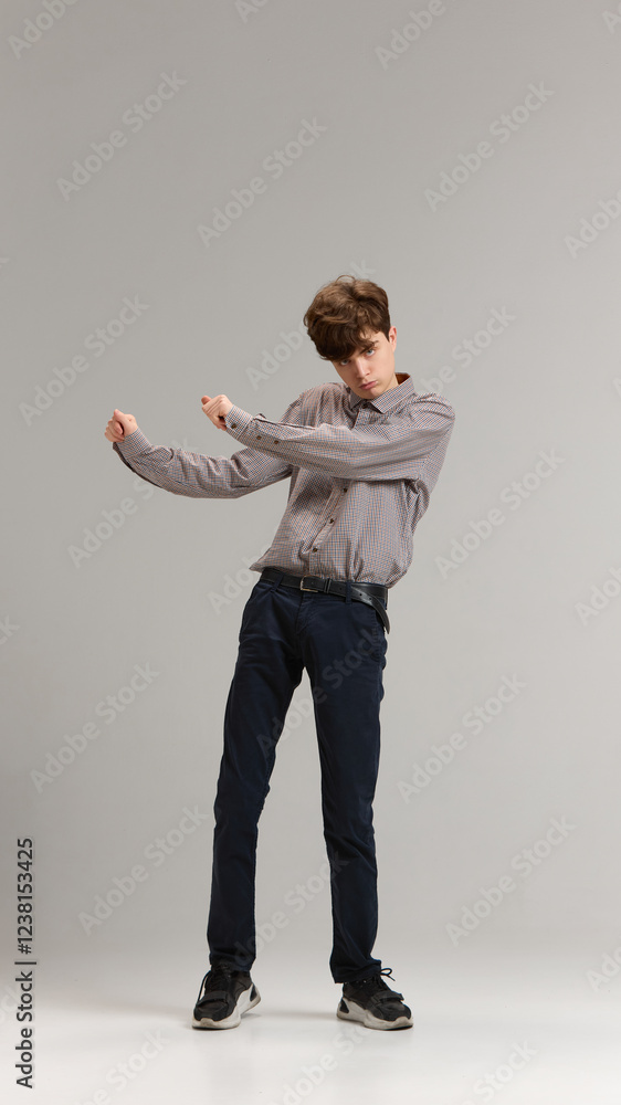 Full-length of teen boy, student in shirt and jeans emotionally dancing in excitement against grey studio background. Concept of youth, education, emotions, happiness Full-length of teen boy, student in shirt and jeans emotionally dancing in excitement against grey studio background. Concept of youth, education, emotions, happiness