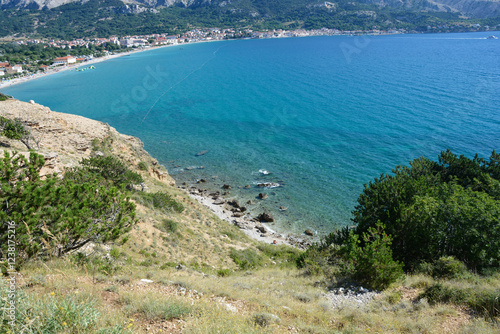 A view of Baska beach (Vela plaza) and the village of the same name, situated by the blue sea, as seen from the rocky western shore of Baska Bay in Croatia photo