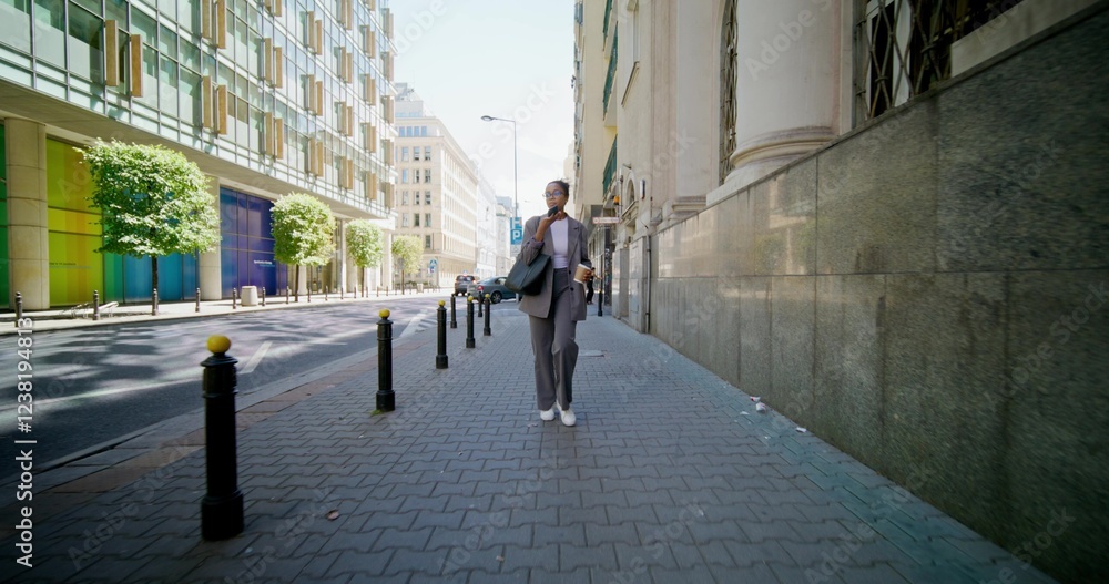 A woman in formal clothes records a voice message on a mobile phone while walking around the city on a sunny day. A woman in formal clothes records a voice message on a mobile phone while walking around the city on a sunny day.