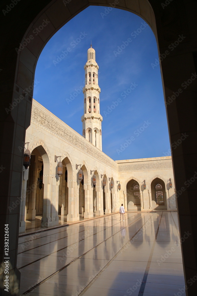 The Sultan Qaboos Grand Mosque in Muscat, Oman, with a courtyard viewed through arcades and the minaret in the background