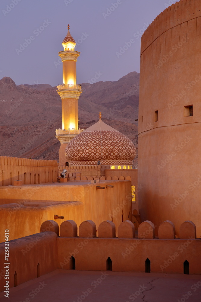 The impressive Nizwa fort in Nizwa, Al Dakhiliyah, Oman, with the minaret of the Mosque in the background. Picture taken during the blue hour