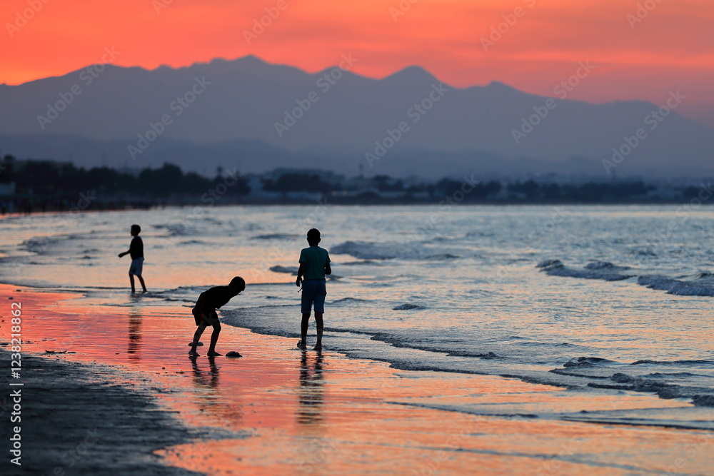 The Qurum Beach in Muscat, Oman at sunset, with a blazing sky and Omani children playing on the seashore