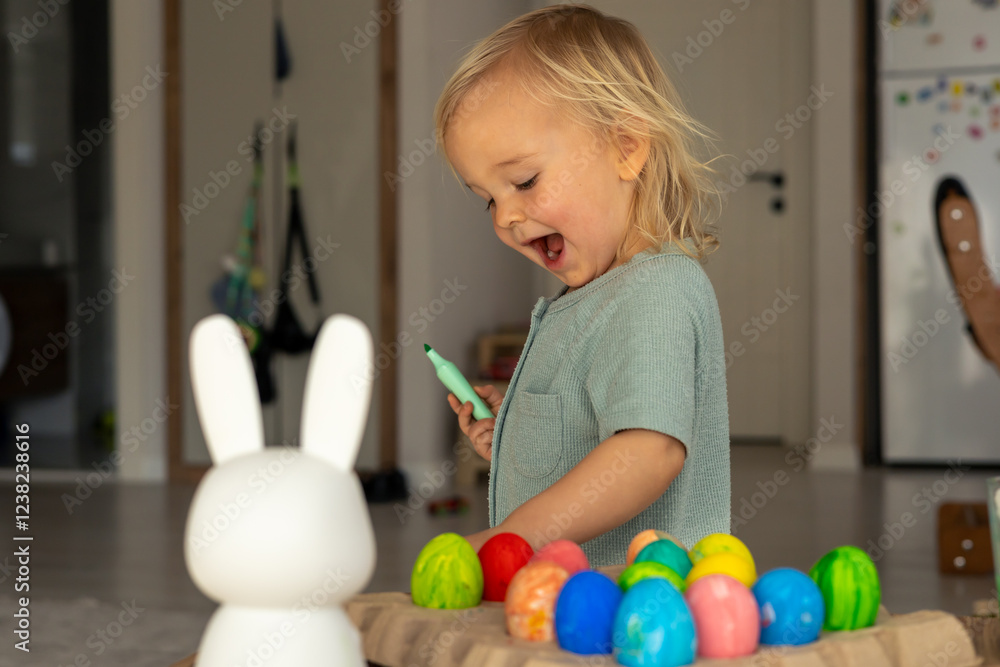 Obraz premium Child joyfully decorating colorful Easter eggs in a bright spring setting at home
