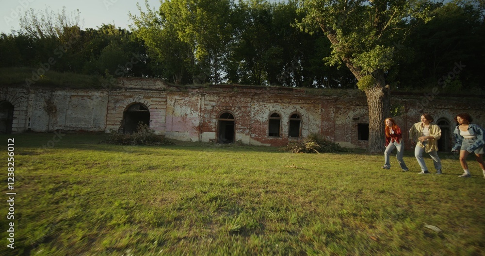 Obraz premium Three young friends are having fun and running around the ruins of a historic building. The fortress walls are overgrown with green vegetation. A sunny summer day