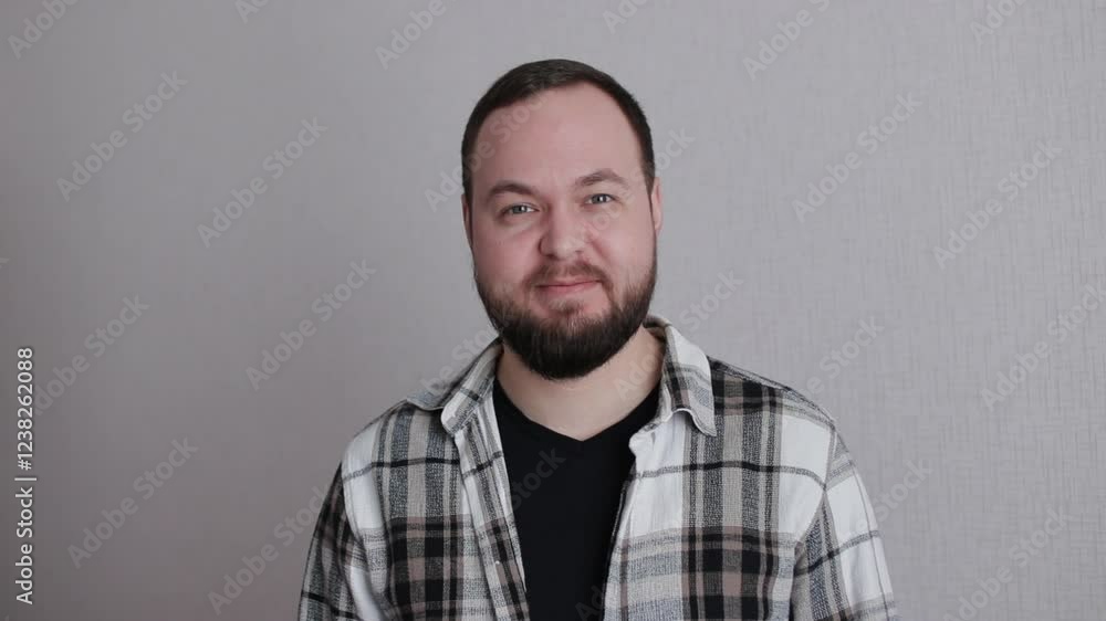 Young and charming bearded man winking at camera isolated on a gray background in a studio Young and charming bearded man winking at camera isolated on a gray background in a studio