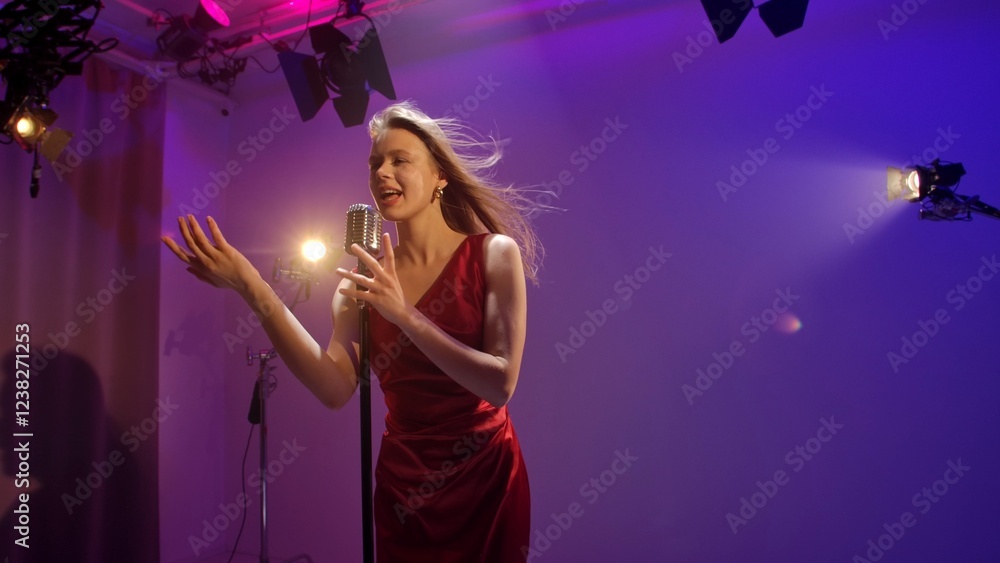 Studio for photo video production filming with lighting equipment and cyclorama, woman singer in red dress singing in retro microphone in neon light. Studio for photo video production filming with lighting equipment and cyclorama, woman singer in red dress singing in retro microphone in neon light.