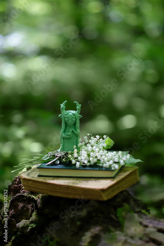 forest spirit figurine, lily of the valley flowers, spell books in forest, natural backdrop. Forest grandmother, defender guardian spirit of nature. witchcraft, green magic, esoteric spiritual ritual photo