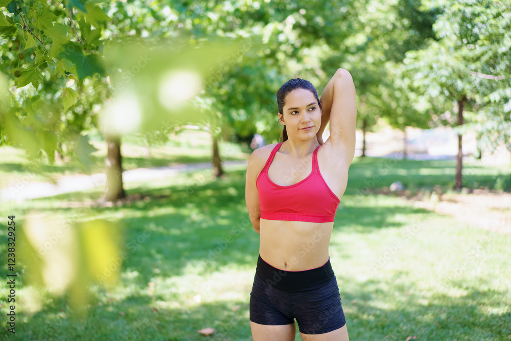 A woman in activewear is stretching outdoors in a park surrounded by greenery, under the warmth of the sunlight A woman in activewear is stretching outdoors in a park surrounded by greenery, under the warmth of the sunlight