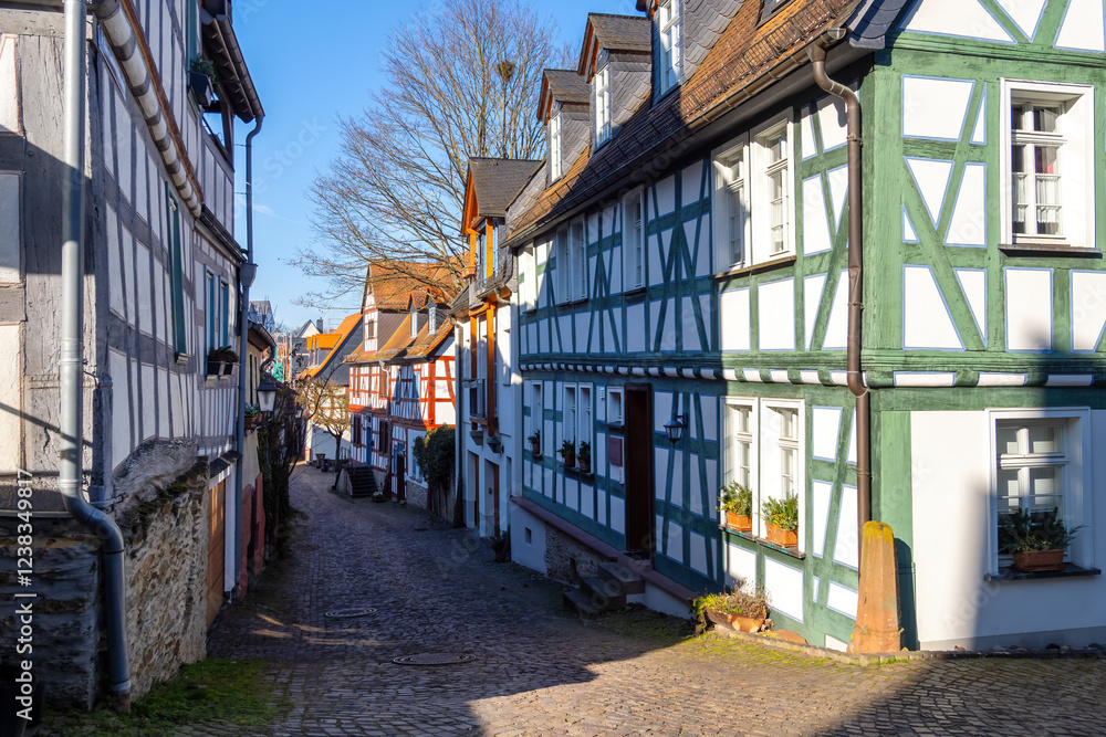 Fototapeta premium Charming cobblestone street showcasing colorful half-timbered houses in the historic down town of Idstein, bathed in warm sunlight