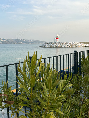 A serene coastal scene featuring a red and white lighthouse, greenery, and calm waters. Perfect for travel, nature, and maritime-themed projects photo