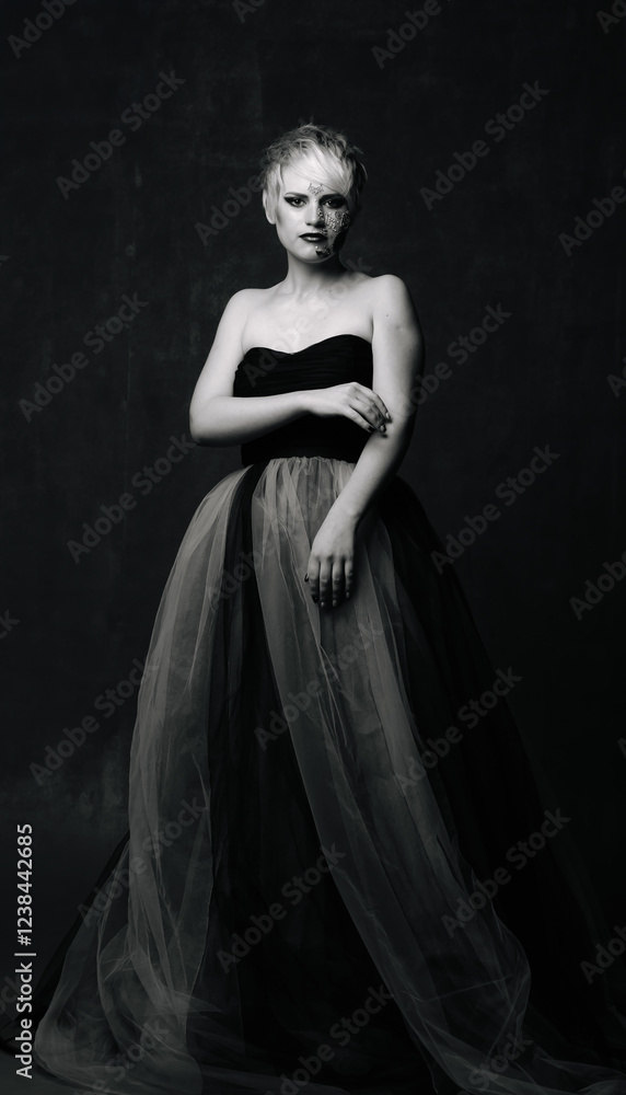 Chic black-and-white model portrait. A model poses gracefully in a black strapless gown, showcasing a striking look in a dark studio setting. Chic black-and-white model portrait. A model poses gracefully in a black strapless gown, showcasing a striking look in a dark studio setting.