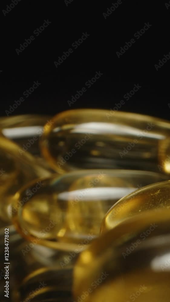 Vertical video. Dolly Slider Close Up of Golden Transparent Omega 3 Capsules Highlighting Their Smooth Glossy Texture and Reflections on a Dark Background Nutritional Supplementation Vertical video. Dolly Slider Close Up of Golden Transparent Omega 3 Capsules Highlighting Their Smooth Glossy Texture and Reflections on a Dark Background Nutritional Supplementation