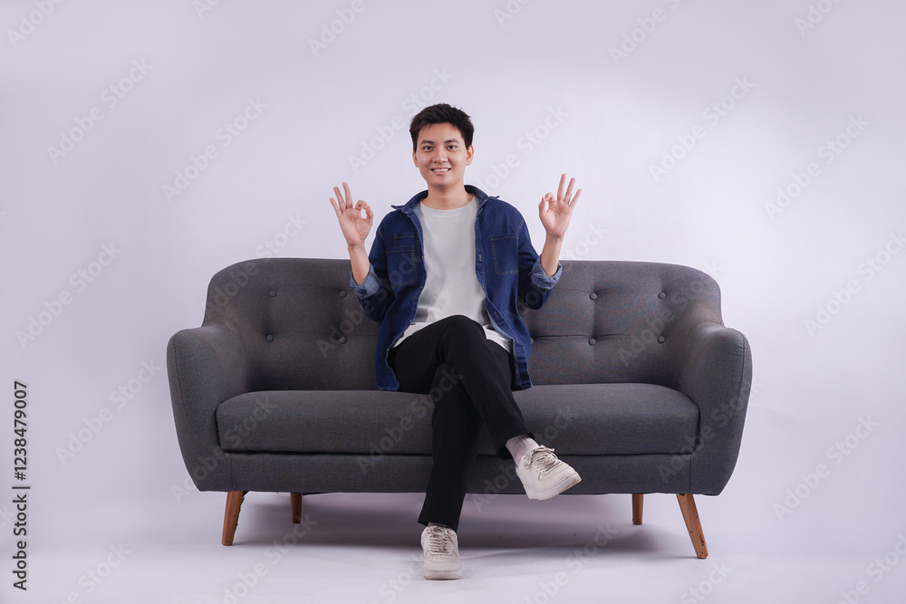Full body image of young Asian man posing on sofa on white background Full body image of young Asian man posing on sofa on white background