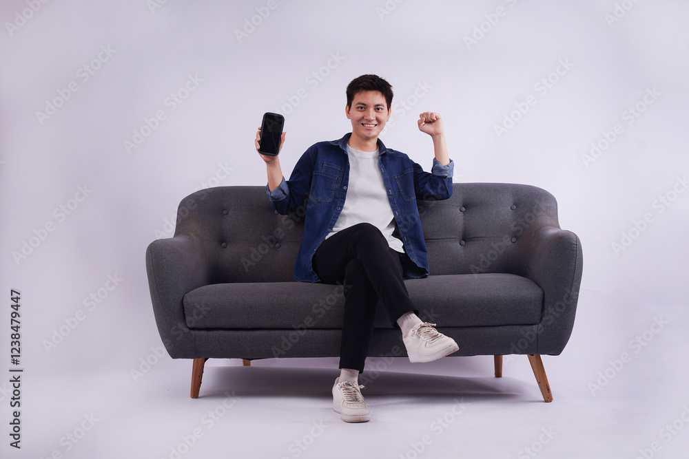 Full body image of young Asian man posing on sofa on white background Full body image of young Asian man posing on sofa on white background
