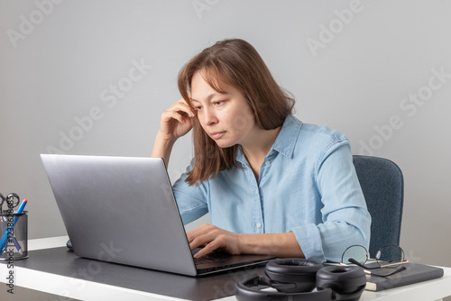 A woman typing on the keyboard using laptop, looking at PC screen, remote hardworking stooped freelancer works from home. Incorrect posture, bad habit to use computer photo