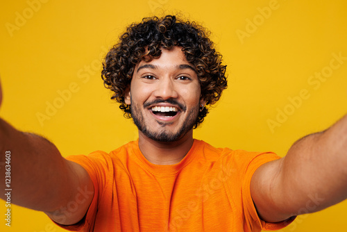 Photography Close up young smiling satisfied happy Indian man wear orange t-shirt casual clothes doing selfie shot pov on mobile cell phone isolated on plain yellow background studio portrait