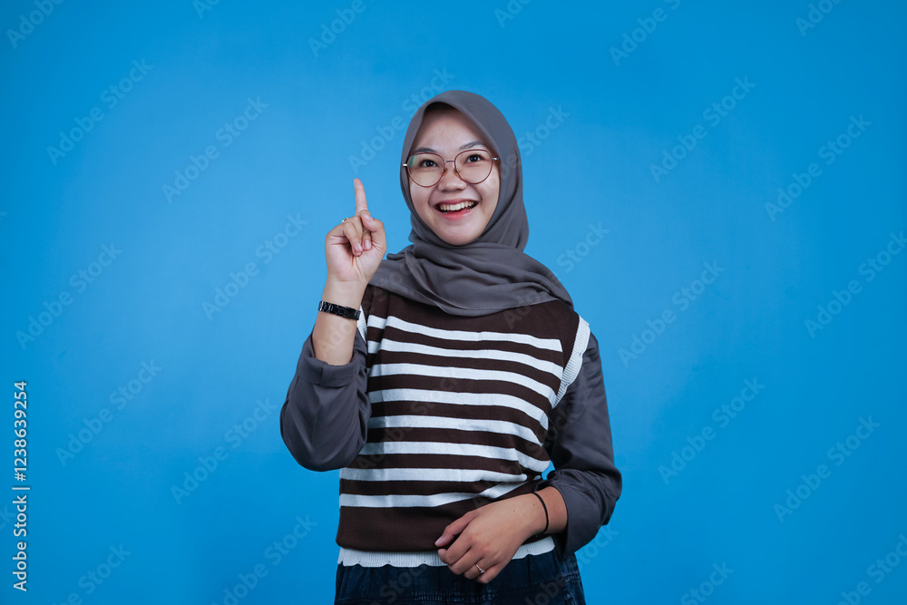 Smiling Young Woman with Finger Pointing Up on Blue Background Smiling Young Woman with Finger Pointing Up on Blue Background