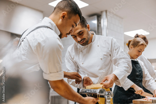 Young male chef using pasta maker with help of coworker in commercial kitchen photo