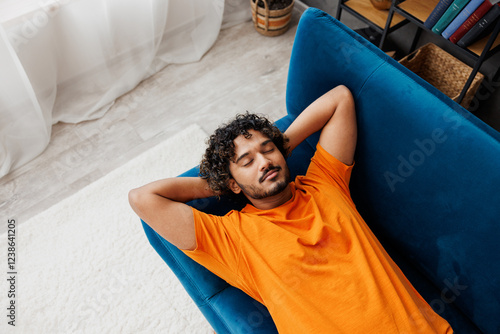 Foto Top view young calm Indian man he wear orange casual clothes lay down on blue sofa couch sleep take nap stay at home hotel flat rest relax spend free spare time in living room indoor