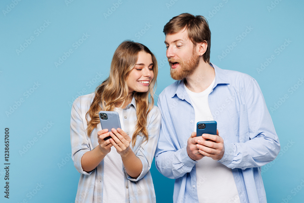 Young curious couple two friend family man woman wear shirt casual clothes together hold in hand use look at mobile cell phone isolated on pastel plain light blue background studio. Lifestyle concept Young curious couple two friend family man woman wear shirt casual clothes together hold in hand use look at mobile cell phone isolated on pastel plain light blue background studio. Lifestyle concept