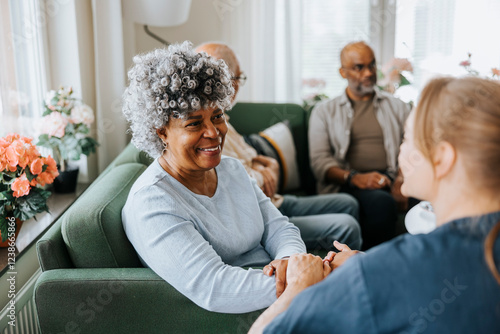 Smiling senior woman sitting on sofa and talking with healthcare expert at nursing home photo