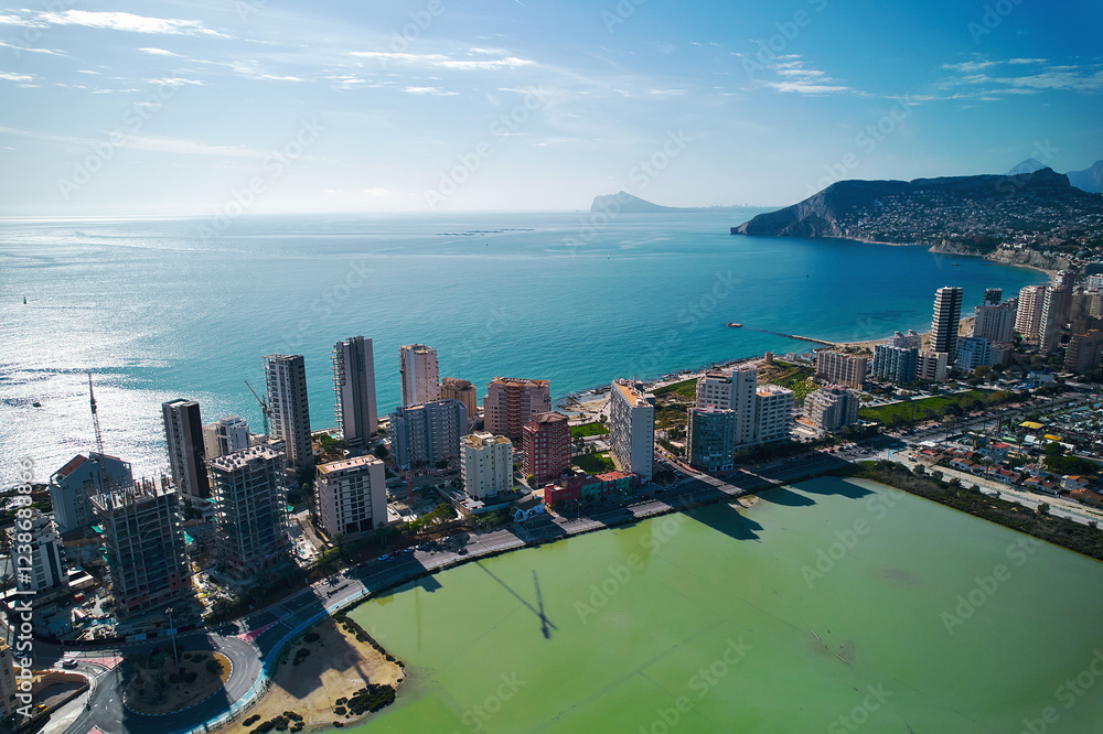 Obraz premium Aerial shot of Calpe cityscape. Costa Blanca, Spain. Coastal town with towering residential and commercial buildings lining salt lake and Mediterranean Sea shoreline. Travel and touristic places conce