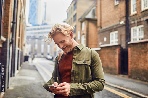 Young redhead man using a smart phone on a city street photo